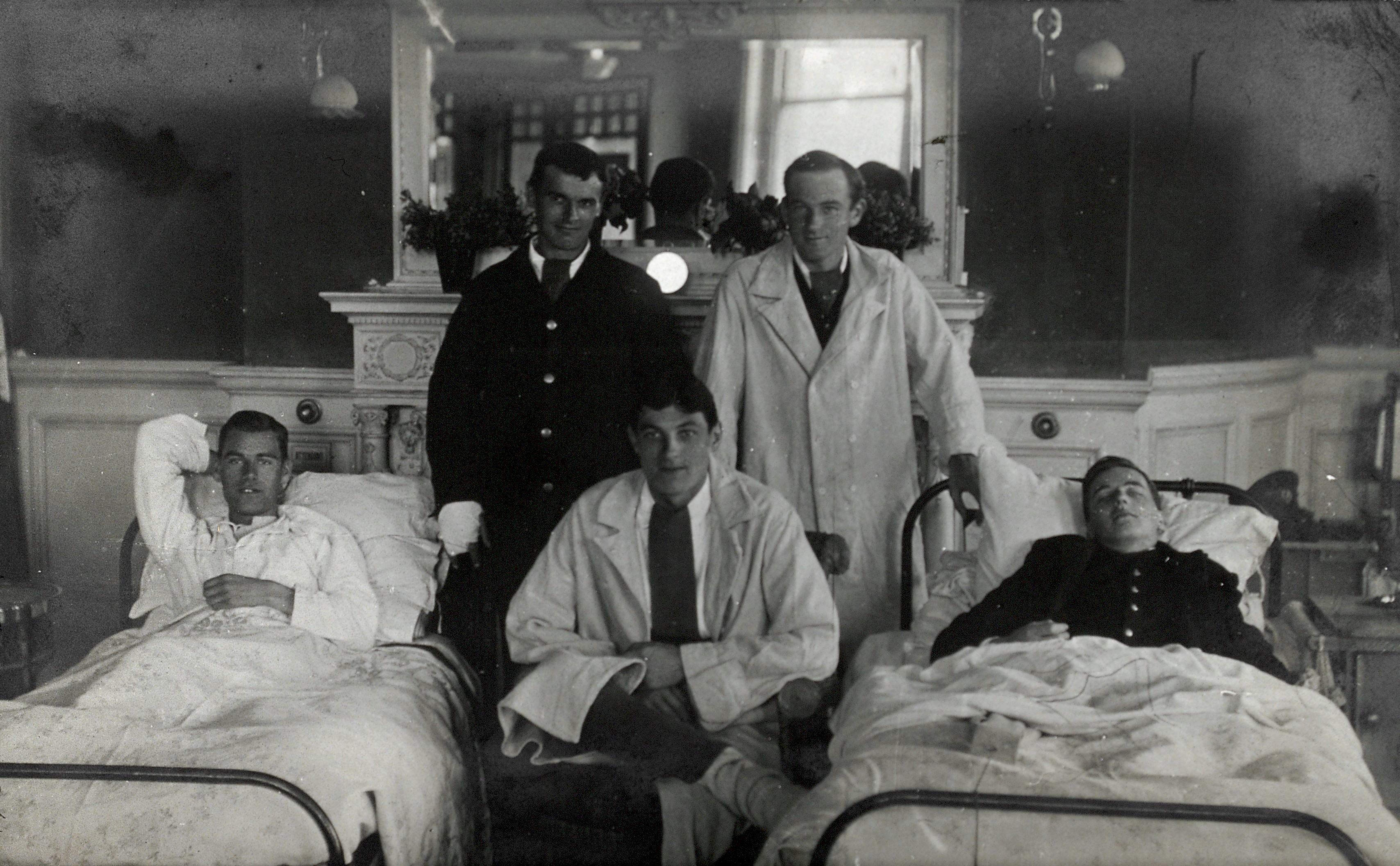 'First World War wounded soldiers, two lying in hospital beds, with medical staff. Photograph, 1914/1918.' . Credit: https://wellcomecollection.org/works/cxmvjutp  | https://creativecommons.org/licenses/by/4.0/