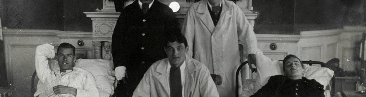 'First World War wounded soldiers, two lying in hospital beds, with medical staff. Photograph, 1914/1918.' . Credit: https://wellcomecollection.org/works/cxmvjutp  | https://creativecommons.org/licenses/by/4.0/